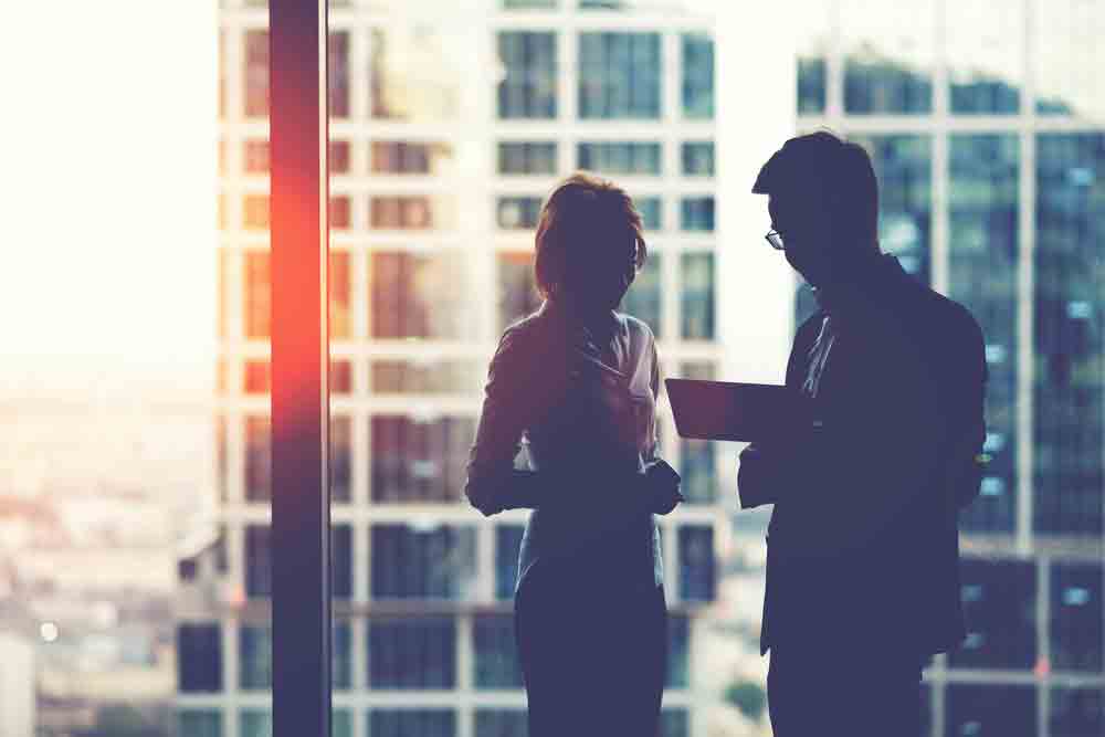 a manager and an employee have a discussion in front of glass windows in a high-rise building